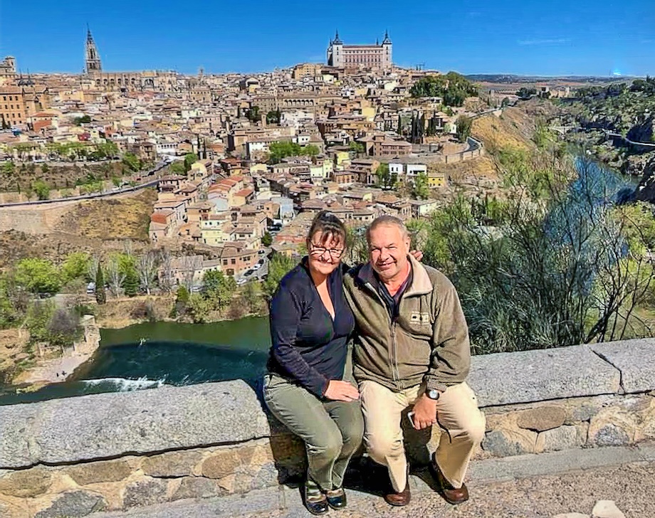 A panoramic vista of the historic old town skyline with Eddie and Marie sitting on a rock wall in the foreground. We were exploring Segovia.