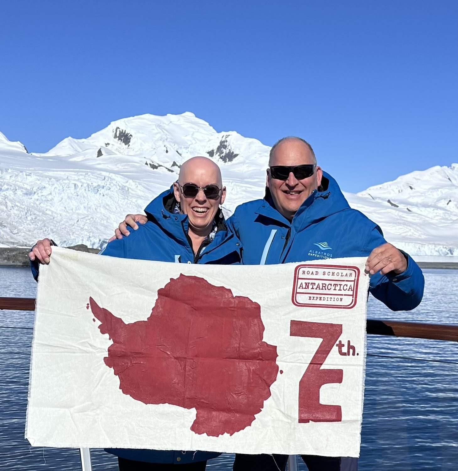 Scott and Donna Paul-Bonham hold up the Antiarctica flag while standing on Red Rock Ridge within the Antarctic Circle.
