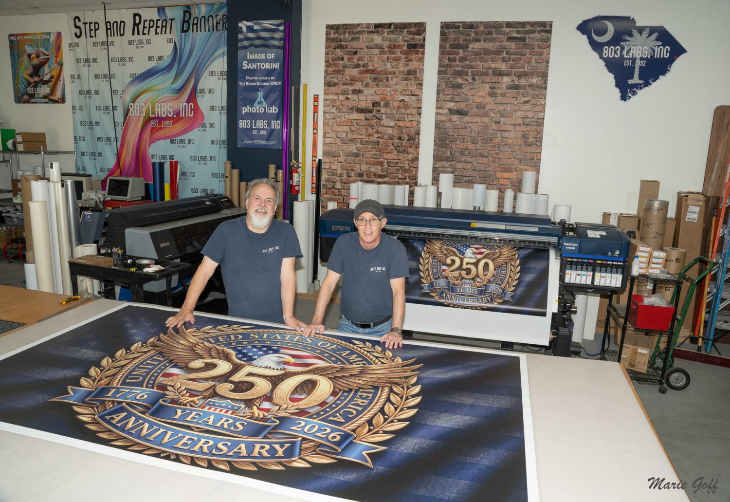 Inside 803 Labs, Inc., where owner Tony and visual artist Rich are standing in front of a banner of the United States of America’s 250th anniversary. Without them, South Carolina’s Revolutionary War Sites would have been difficult.