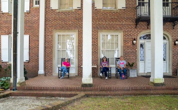 Hobcaw barony expansive veranda with three people sitting in the rocking chairs.