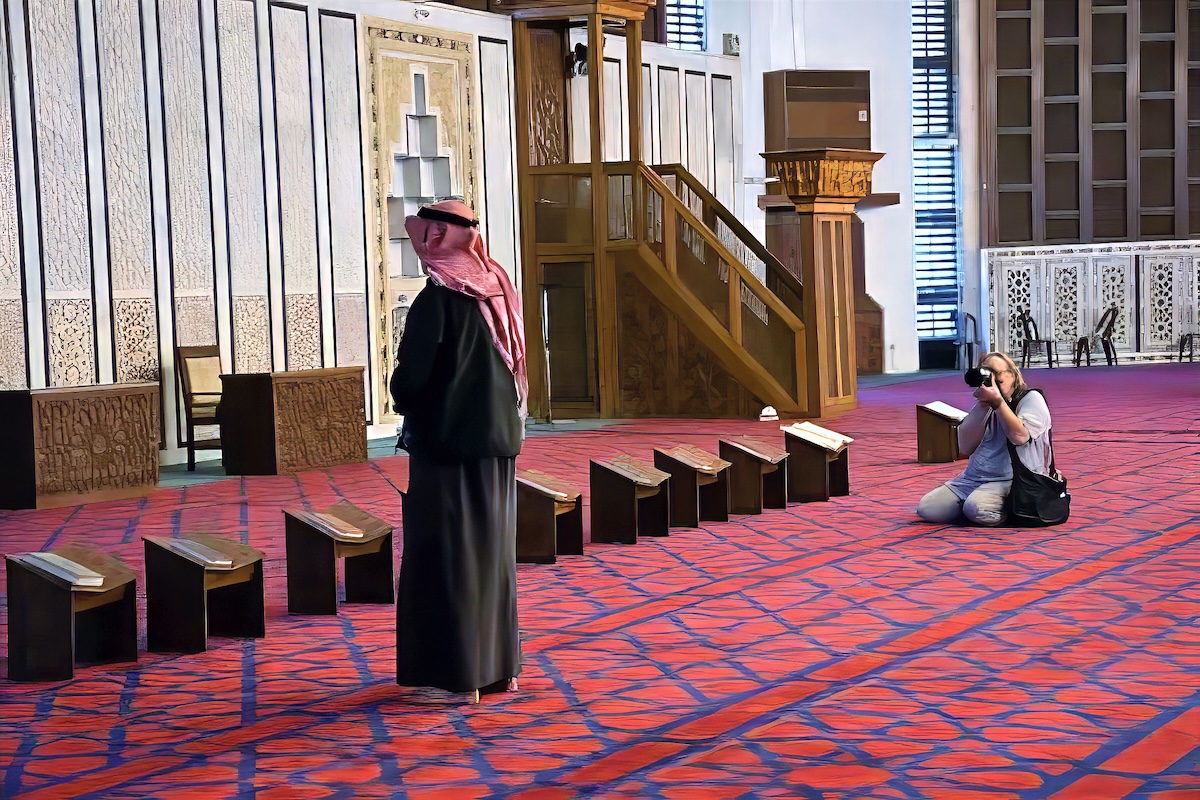 a Mosque in Jordan wiht a person standing and a photographer kneeling on the floor.