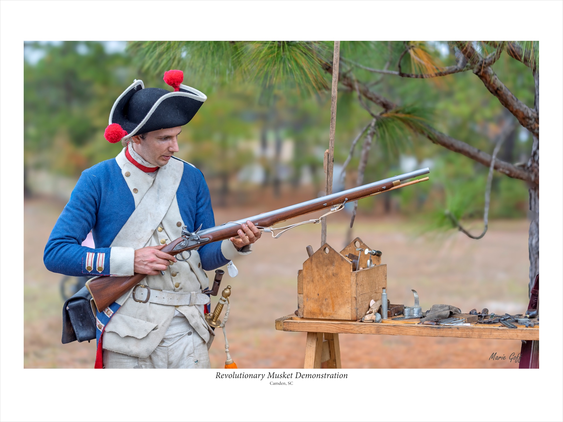 A reenactor is holding a musket and has his tools laid out on a table beside him.