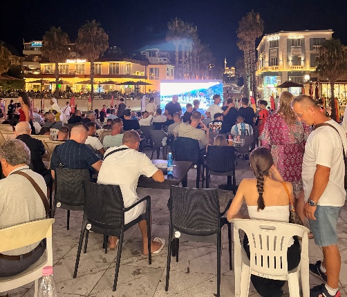 Durrës City Center Albania at night with a jiant outdoor screen and people gathered at table to see the Word Cup.