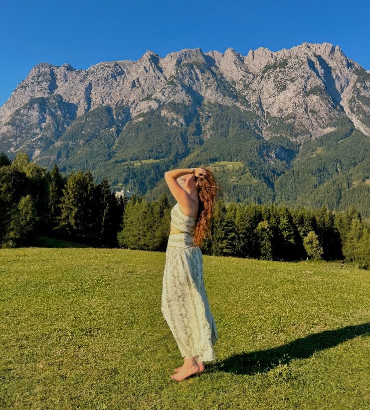 Traveler Meredith Carroll, who wrote 'A Backpack full of Memories', stands in the Austrian Alps, arms raised, hands in her long hair.
