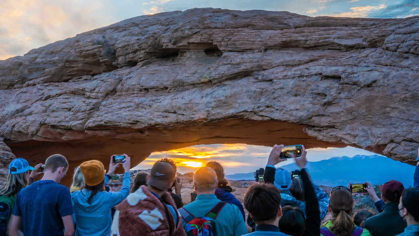 Southern Utah Road Trip Mesa Arch at Canyonlands National Park at daybreak with people in front of it taking pictures with their cell phones.